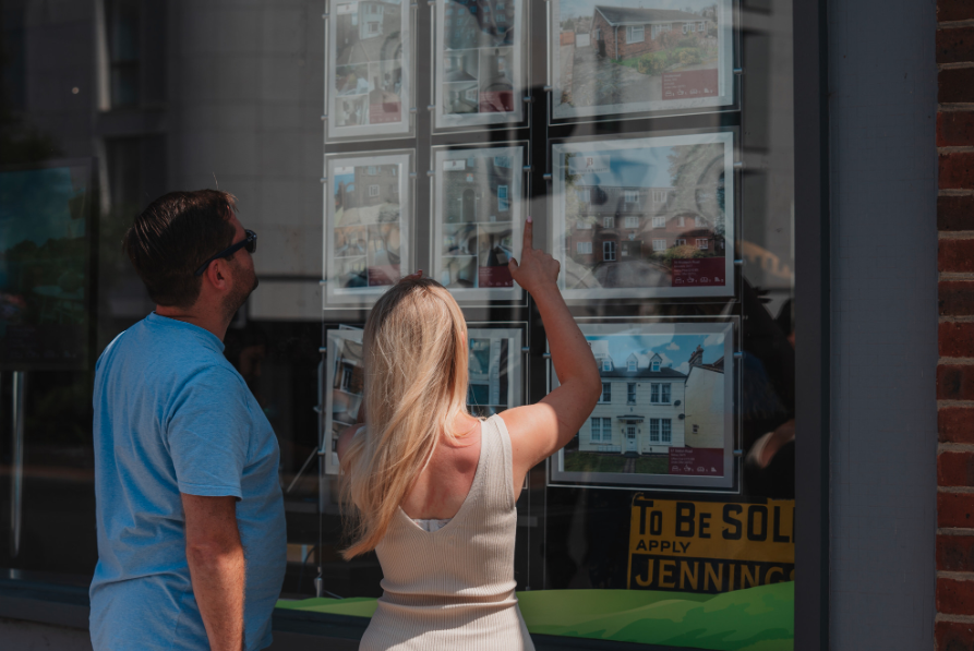 A man and a woman are standing outside of the Jennings & Barrett office looking at property adverts in the office window