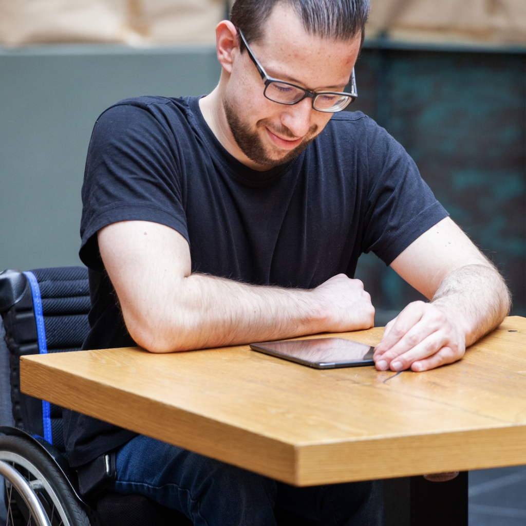 A man using a wheelchair is smiling as he uses his tablet to notify Jennings & Barrett about his Personal Emergency Evacuation Plan (PEEP) requirements