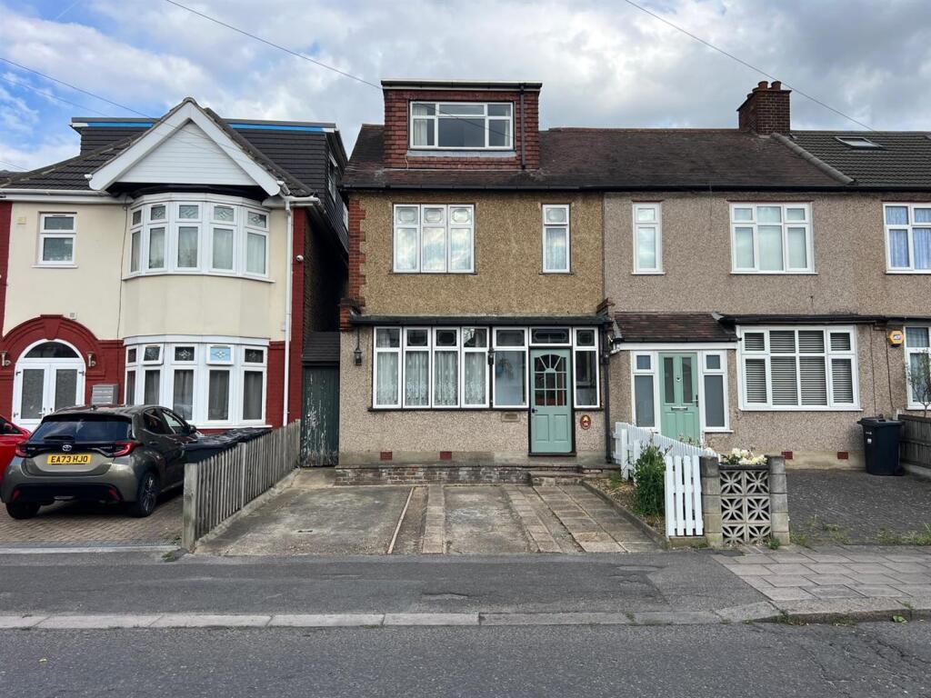 A light brown house with a green door. There are mismatched fences either side and the drive and the side gate both look like they could use some maintenence