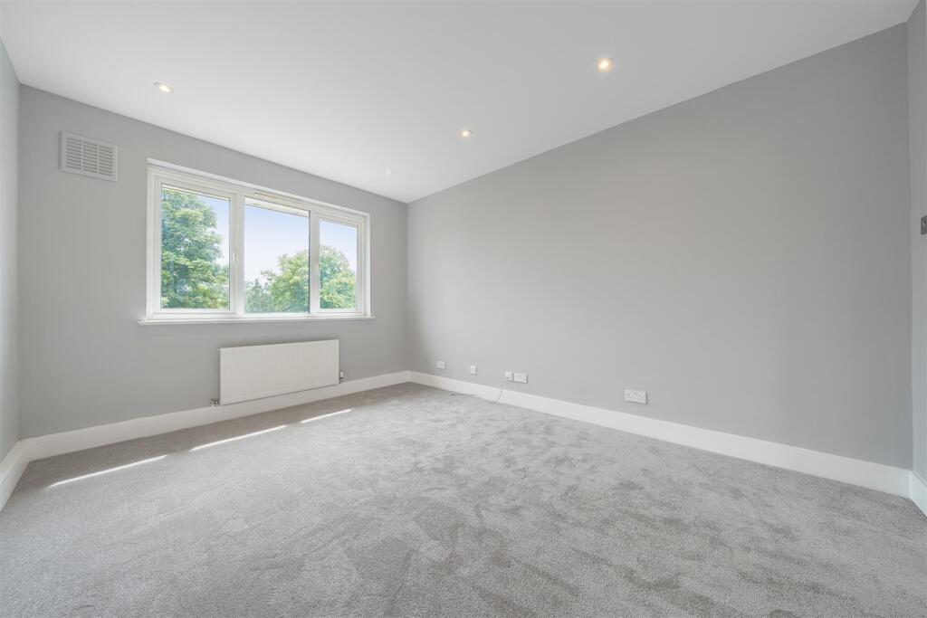 Large empty room with grey walls and carpet. A radiator sits underneath the window