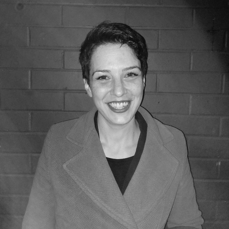 A black and white photo shows Sara smiling into the camera. She is wearing a blazer.