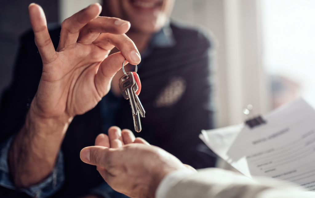 A landlord or agent is handing keys over to a man who is holding a tenancy agreement.