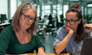 Two female property professionals sit at a desk looking at floorplans.