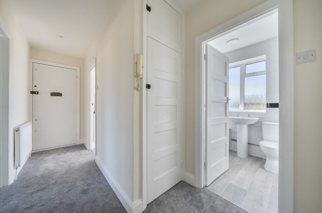 Hallway shows doors into the bathroom and towards the apartment/flat front door. A storage cupboard is centered inbetween.