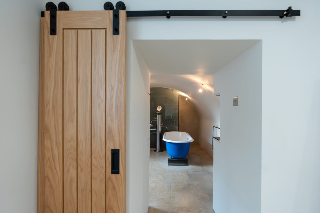 A barn style door hides the beautiful "spa style" family bathroom, with freestanding bath. The bath has a unique blue steel design. Curved ceilings can be seen above the bathroom.