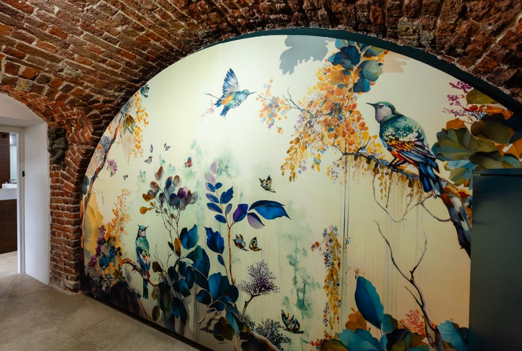 The entrance greets guests with a splash of vibrant colour, thanks to it's stunning bird and foliage mural feature wall. Arched ceilings peek into the photo, their exposed brickwork creating an asymmetrical frame for the photographh.
