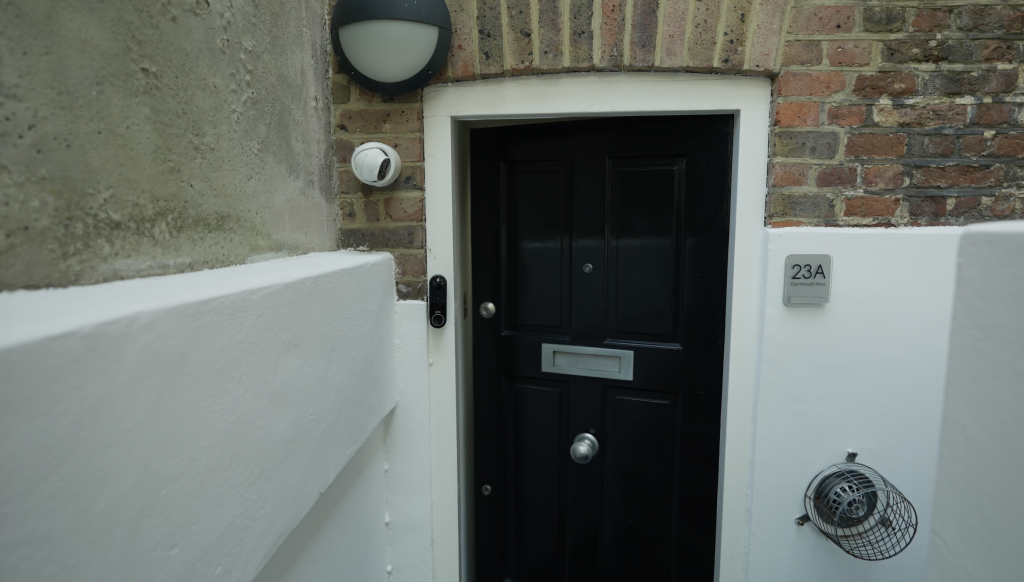 Private entrance to the apartment shows a black, Georgian style front door with high letter box. It is surrounded by white stone work and set into the red brick of the building's exterior.