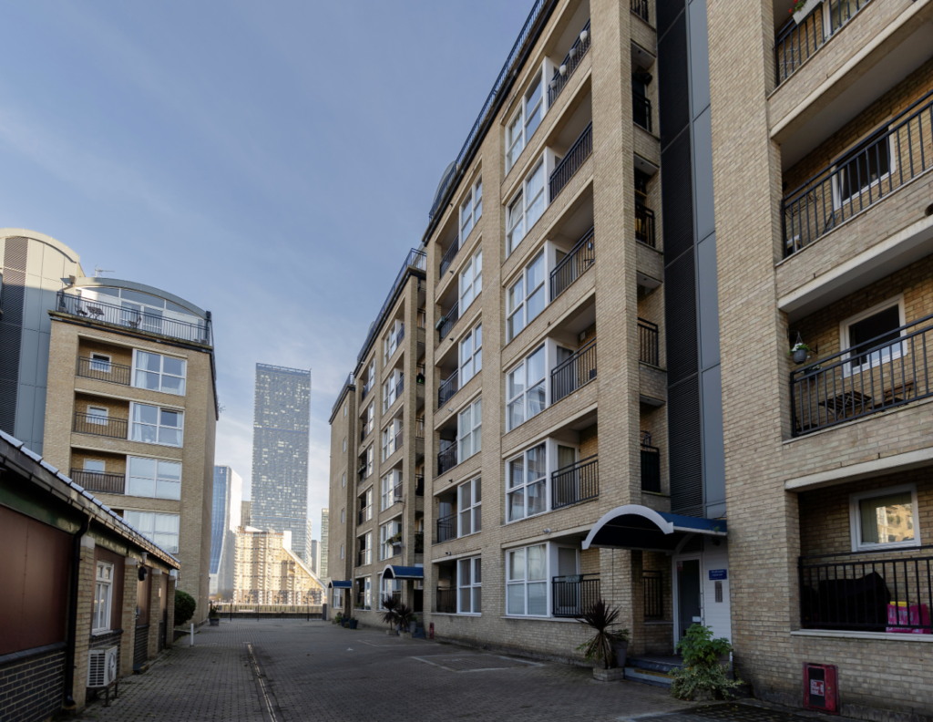 A picture taken from within the development shows the residential buildings lining a road, leading towards a sky scraper